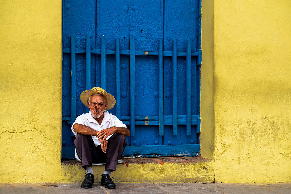 Ein älterer Kubaner sitzt vor einer Tür und raucht eine Zigarre, Trinidad, Provinz Sancti Spiritus, Kuba, Westindische Inseln, Karibik, Mittelamerika