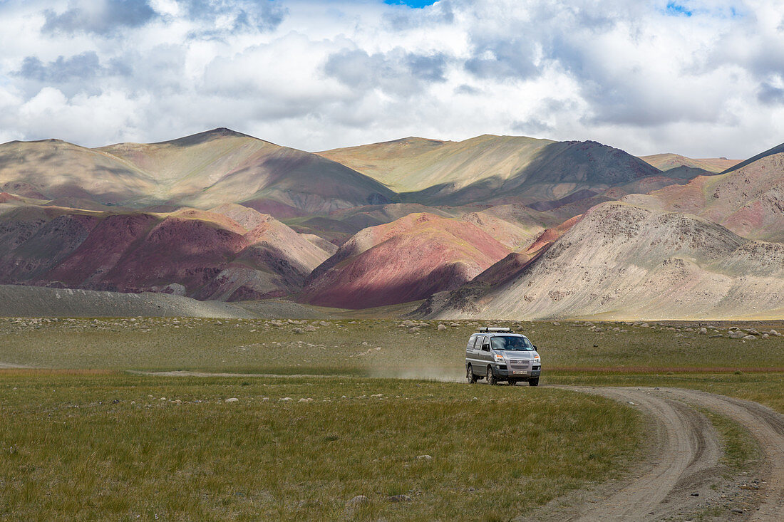 Jeep auf einem Weg am Fuss der teilweise beleuchteten Roten Berge, Tavan Bogd Massiv, Altai, Provinz Bayan-Olgii, Mongolei