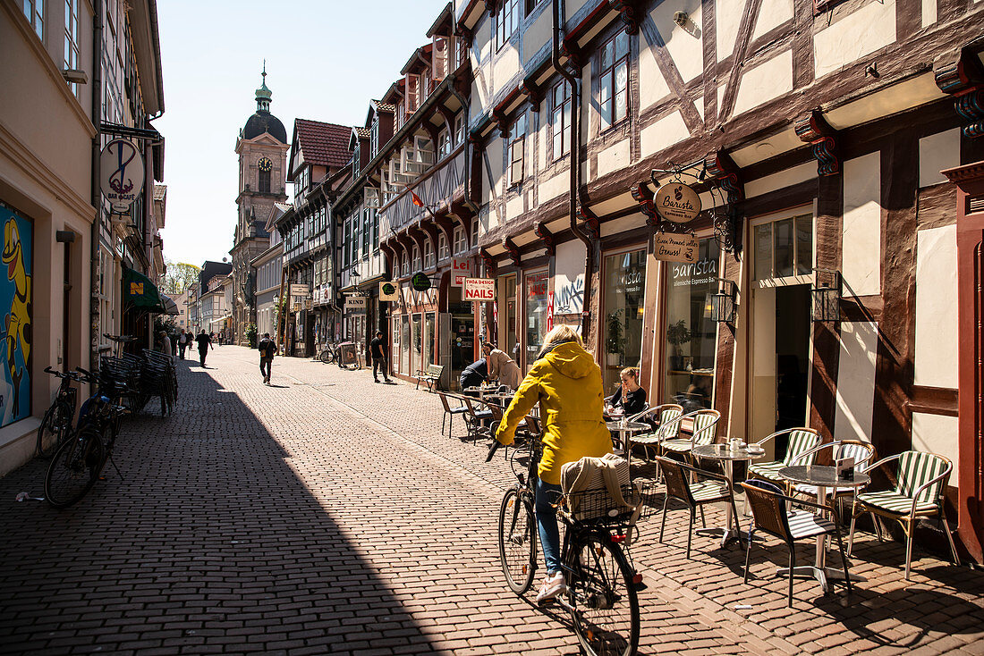 A cyclist in a yellow jacket leads towards the Sankt-Michael church through a half-timbered street with shops, Short Street, G? Ttingen, Lower Saxony, Germany, Europe