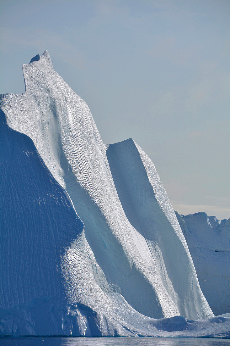 Disco bay; West Greenland; Iceberg in the Kangia Icefjord near Ilulissat; impressive ice formation; towering steep wall with scale-like surface; Ice surfaces shine in the sun; smooth transitions; blue sky and sunshine