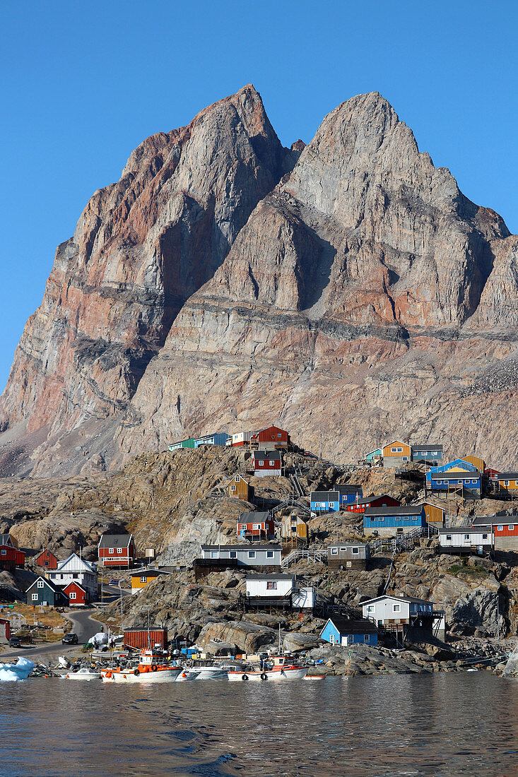 Uummannaq Island in West Greenland; homonymous place below the heart-shaped mountain; &quot;Uummannaq&quot; is the name of the seal heart; View of the with harbor and colorful apartment buildings; Houses stand on rocky, steep terrain;