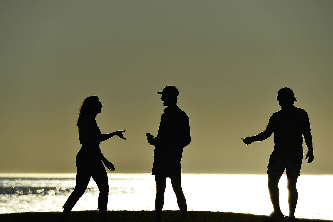 Drei junge Menschen als Silhouetten im Gegenlicht am Pazifik, Santa Monica, Kalifornien, USA