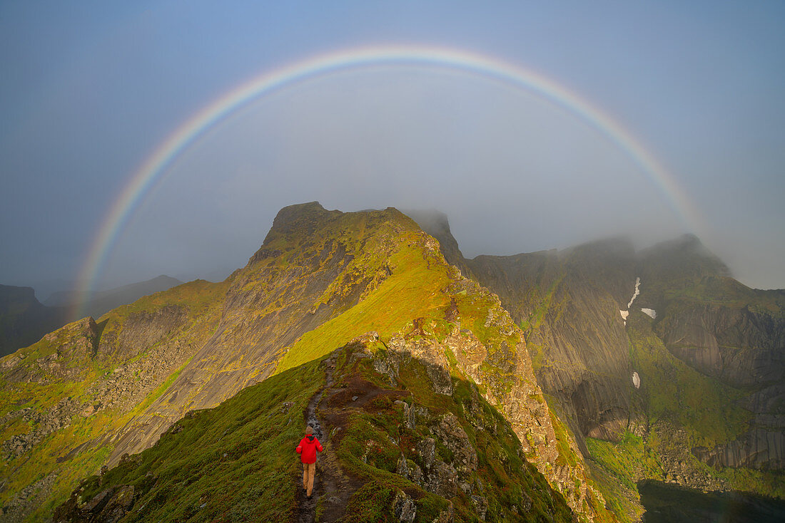 Mann klettert Richtung eines Regenbogens in den Lofoten-Inseln