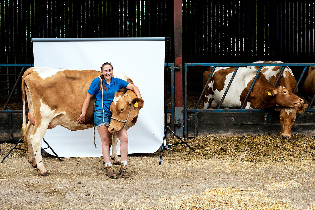 Portrait of female farmer standing in front of a barn with a Guernsey cow.