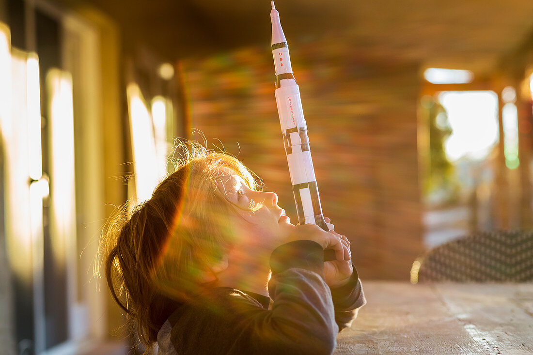 A boy playing with a toy Nasa Saturn 5 rocket, day dreaming about space flight.