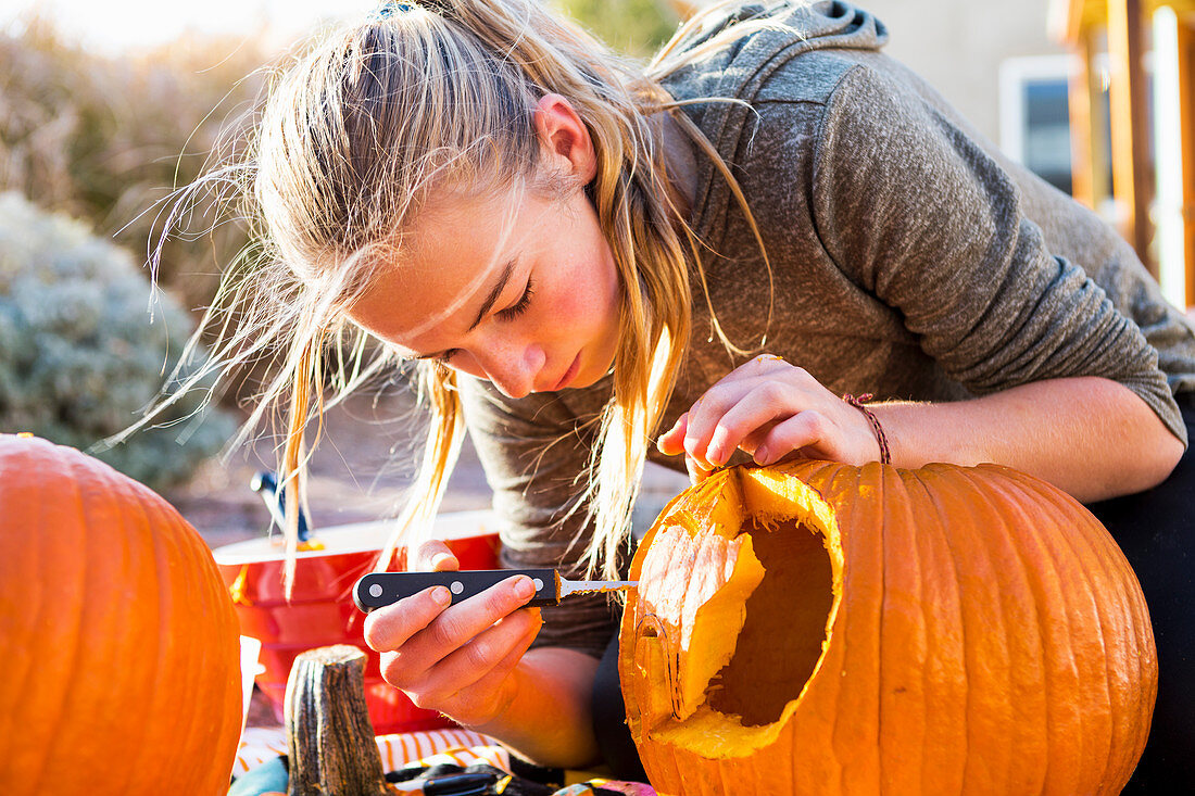 A teenage girl carving a large pumpkin at Halloween.