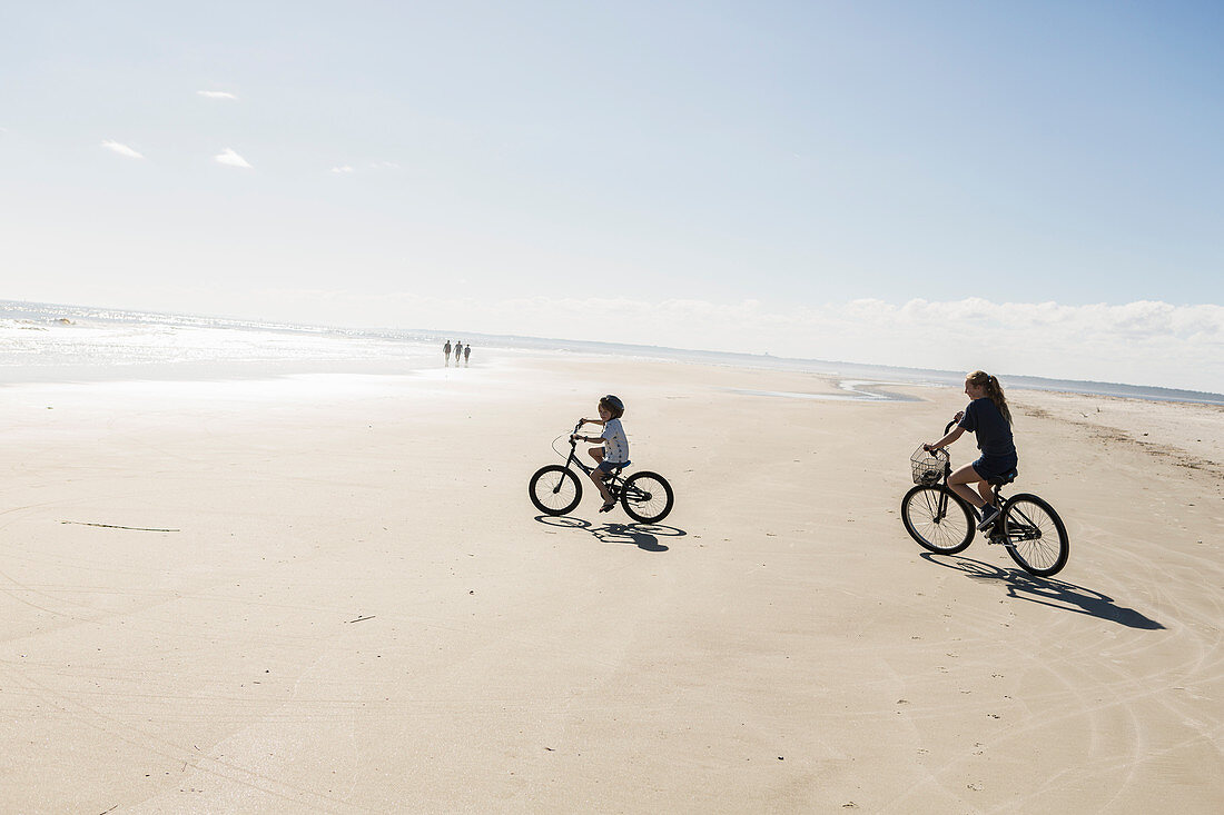 Two children cycling on an open beach, a boy and girl.
