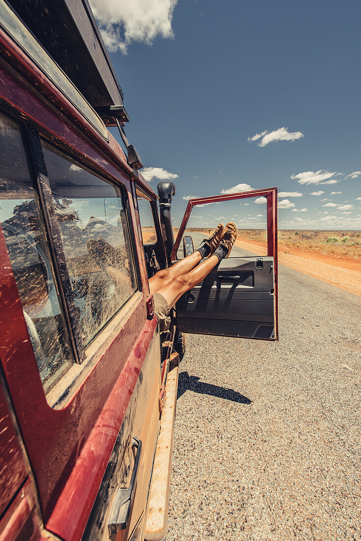 Feet hanging out of an off-road vehicle on a deserted road in the outback in Western Australia, Australia, Oceania;