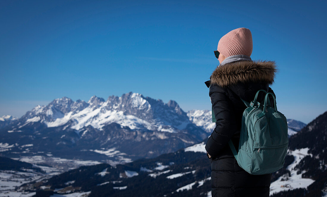 Frau mit Mantel und Mütze mit Blick auf Ellmauer Halt in Fieberbrunn, Kaisergebirge bei Winter, Tirol, Österreich