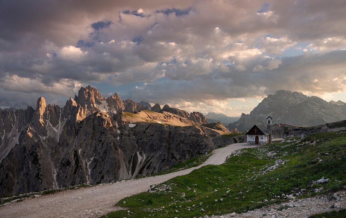 Berglandschaft in den Dolomiten unterhalb der Drei Zinnen mit Kapelle und Weg im Sonnenuntergang, Südtirol