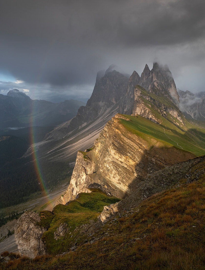 Gebirgsflanke Seceda mit dichten Wolken, Sonne und Regenbogen in den Dolomiten bei St. Ulrich, Südtirol