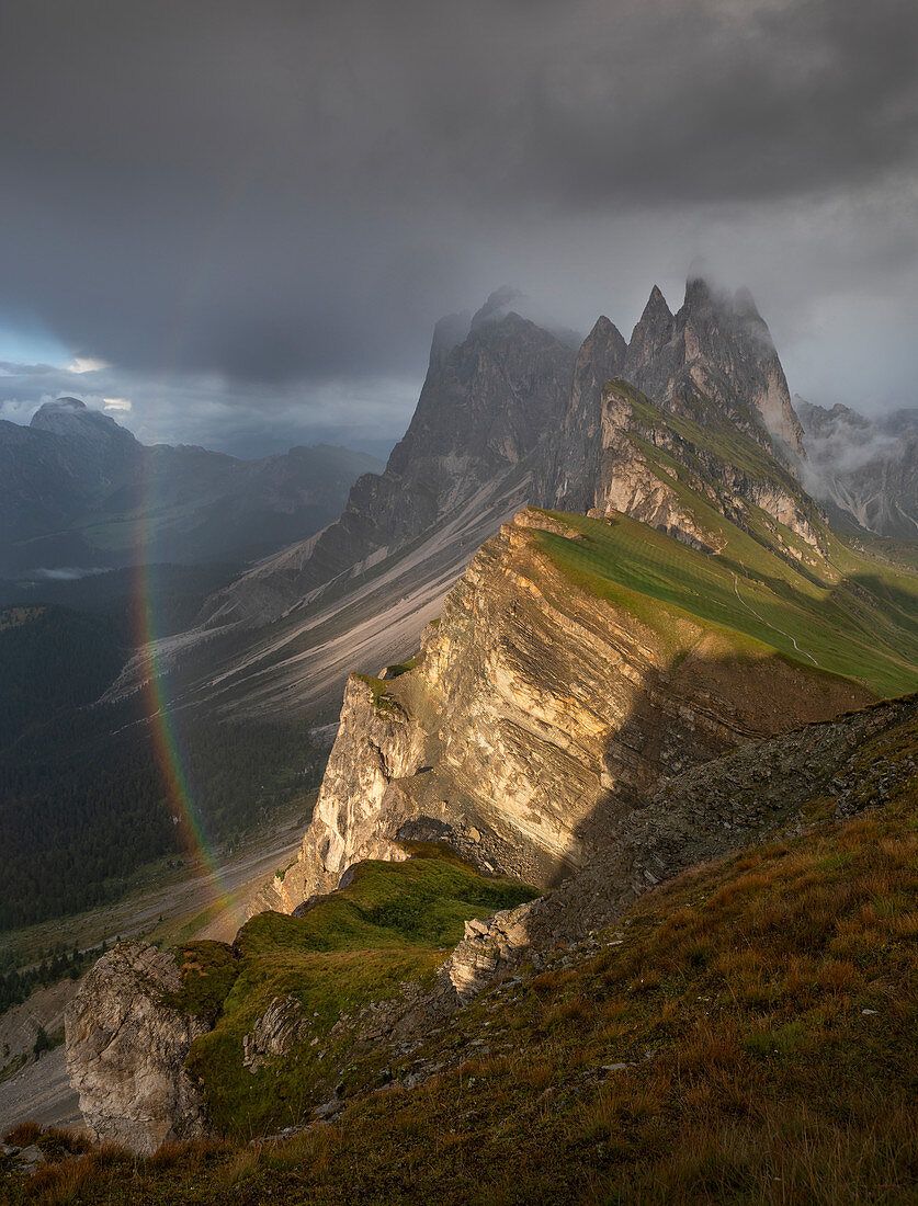 Seceda mountainside with thick clouds, sun and rainbow in the Dolomites near Ortisei, South Tyrol