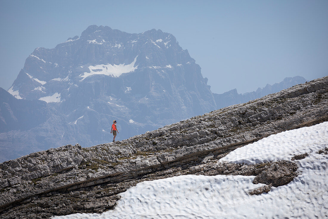 Frau wandert über Felskante, Gebirge der Dolomiten im Hintergrund, mit Schneefeld, Cinque Torri Südtirol