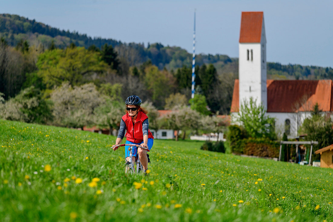 Frau beim Radfahren vor Kirche von Kematen, Baum-zu-Baum-Radweg, Oberbayern, Bayern, Deutschland