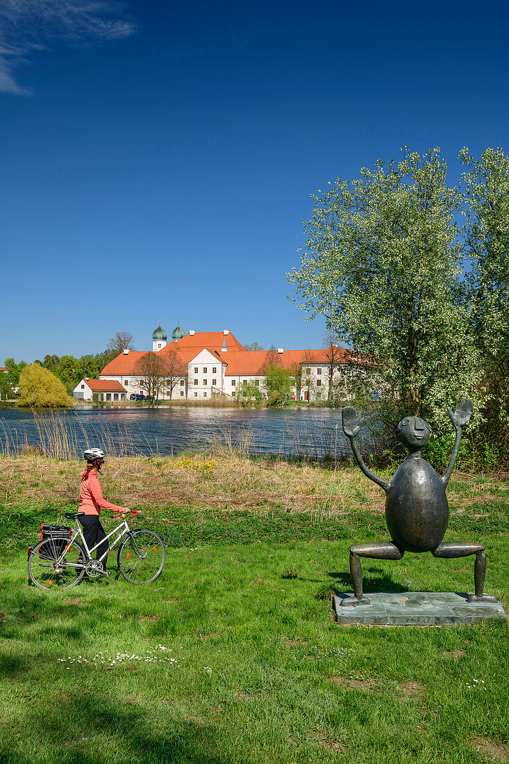 Woman cycling in front of Klostersee and Kloster Seeon, Kloster Seeon, Benediktradweg, Chiemgau, Upper Bavaria, Bavaria, Germany