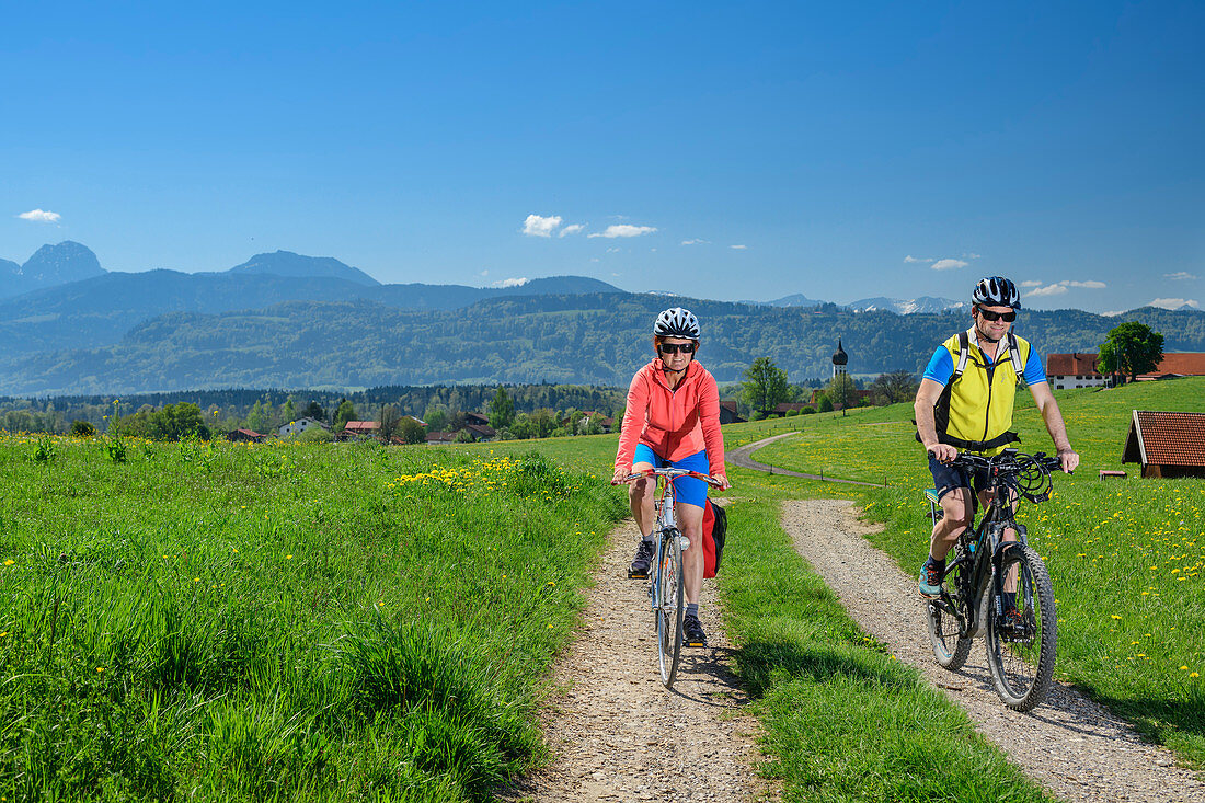 Woman and man cycling, village and Mangfall mountains in the background, Bad Aibling, Upper Bavaria, Bavaria, Germany