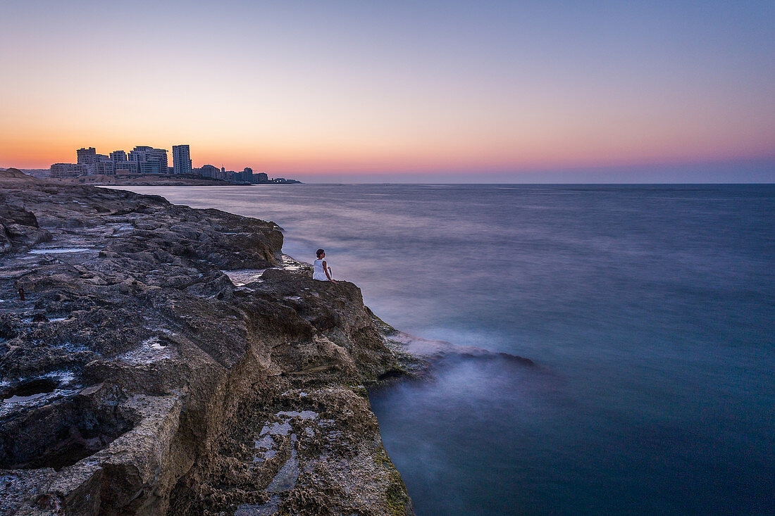 Frau sitzt auf den Steinen außerhalb der Stadtmauern von Valletta und genießt den Sonnenuntergang