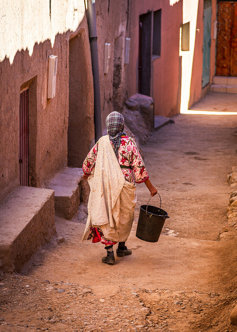 Local people carry a bucket through the streets of Tinghir, Morocco