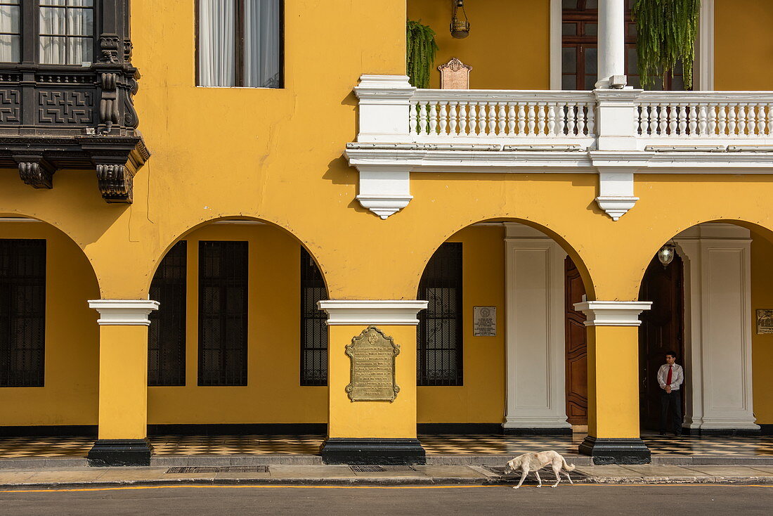 Ein Hund schleicht an einem atemberaubenden Kolonialpalast auf dem zentralen Platz (Plaza Mejor) in der Innenstadt von Lima vorbei, Lima, Peru, Südamerika