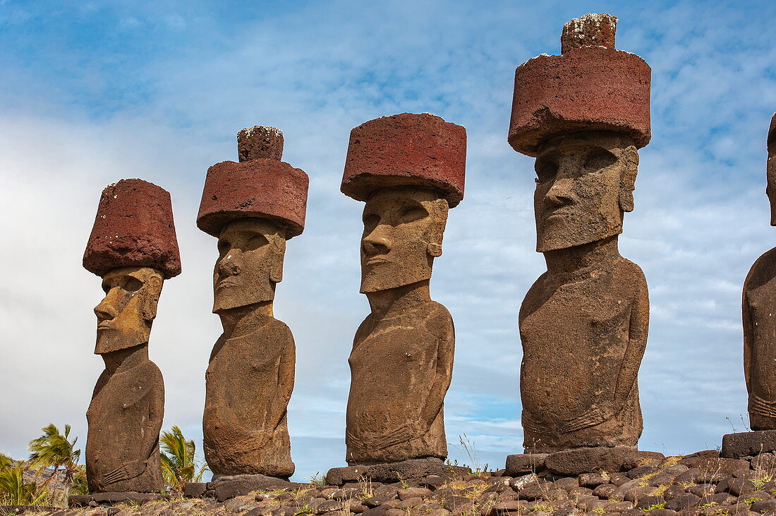A person in the foreground is overshadowed by a group of Moais standing on a ceremonial stone or Ahu from 1250 to 1500, Rapa Nui, Easter Island, Chile