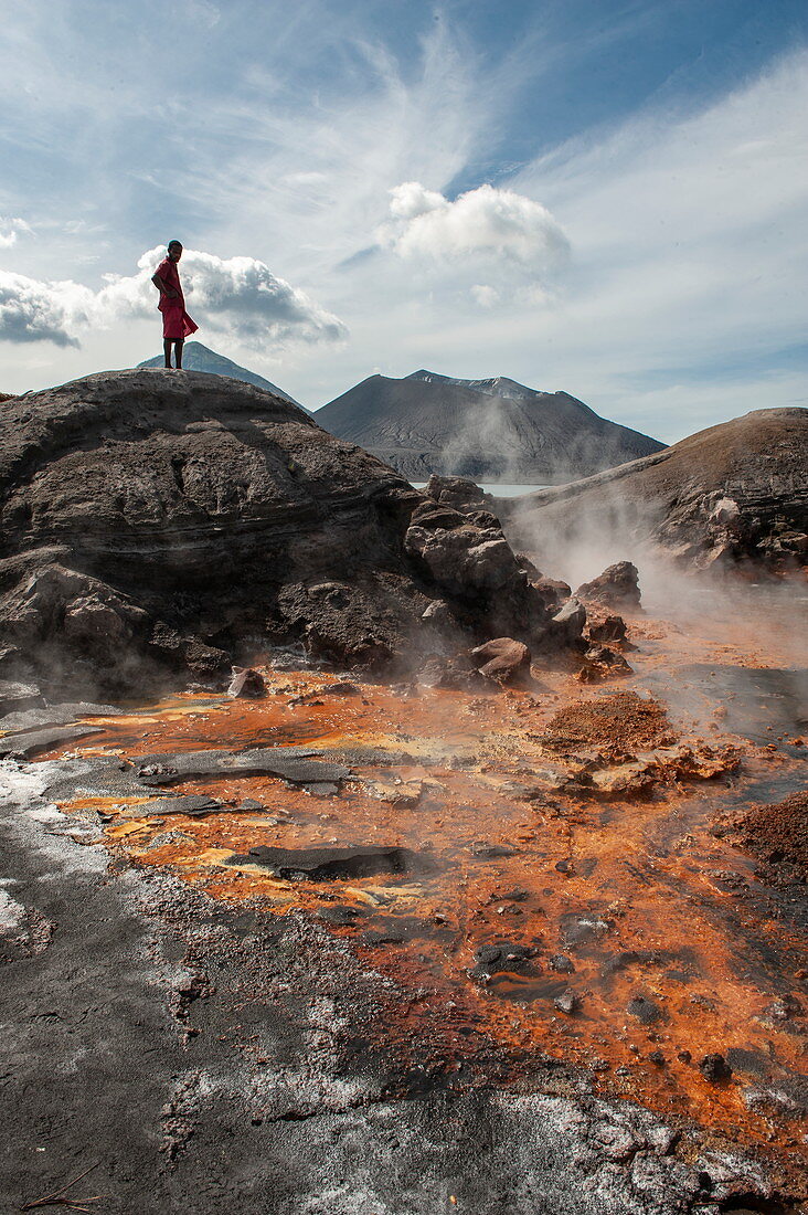 Mann steht auf Felsen und betrachtet Vulkanlandschaft mit orangefarbener Erde und heißen Quellen in der Nähe eines aktiven Vulkans, Rabaul, Provinz Ost-New Britain, Papua-Neuguinea, Südpazifik