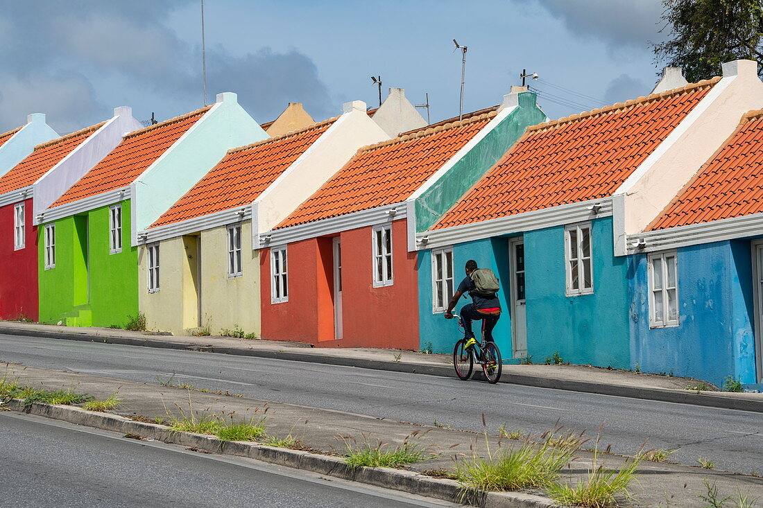 A cyclist passes a row of colorful houses, Pietermaai neighborhood, Willemstad, Curacao, Netherlands Antilles, Caribbean
