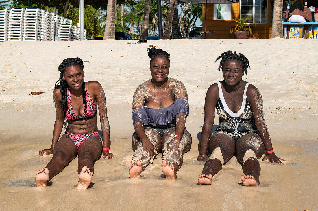 Three smiling young women sitting on the beach, Pigeon Point, Tobago, Trinidad and Tobago, Caribbean