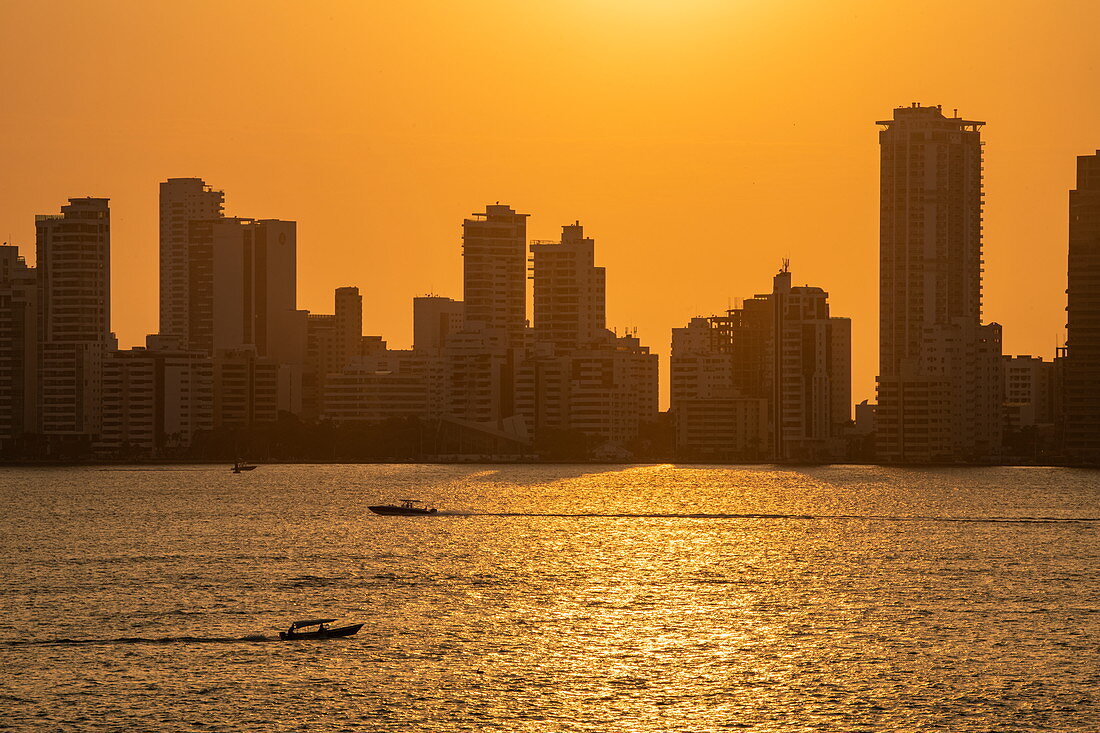 Silhouette von modernen Skylines mit vorbeifahrenden Vergnügungsbooten bei Sonnenuntergang, Cartagena, Bolivar, Kolumbien, Südamerika