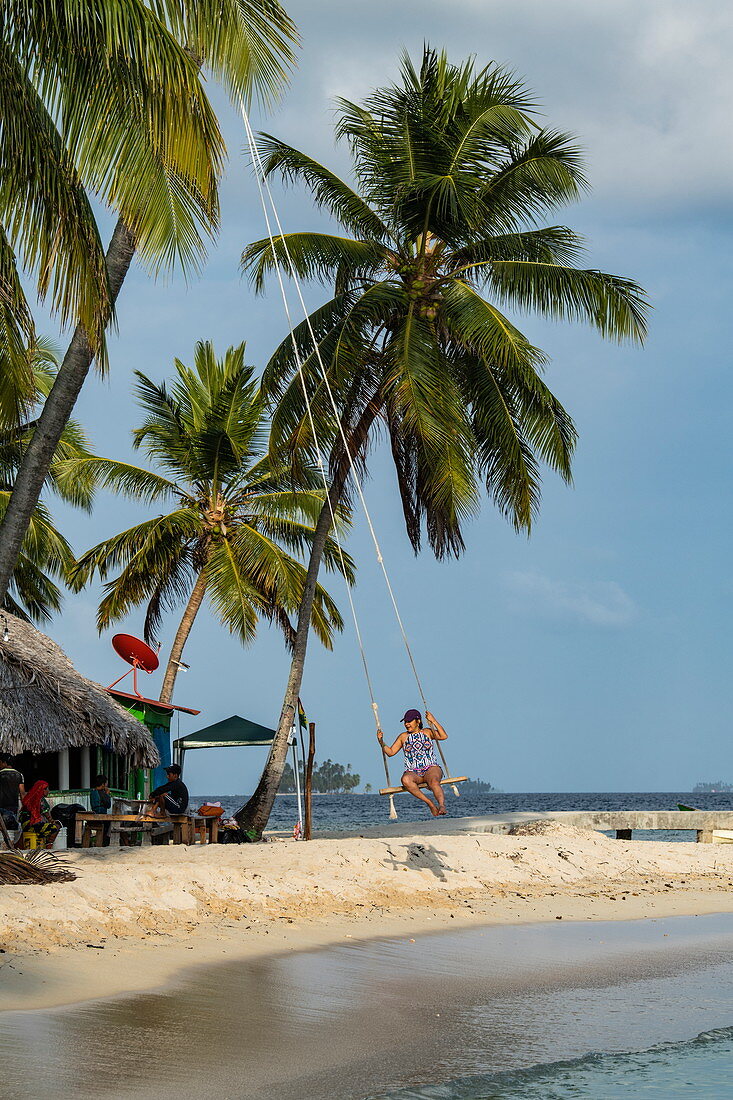 Eine Frau schaukelt am Strand auf einer Schaukel, die an eine Palme gebunden ist, Isla Aroma, San Blas Inseln, Panama, Karibik
