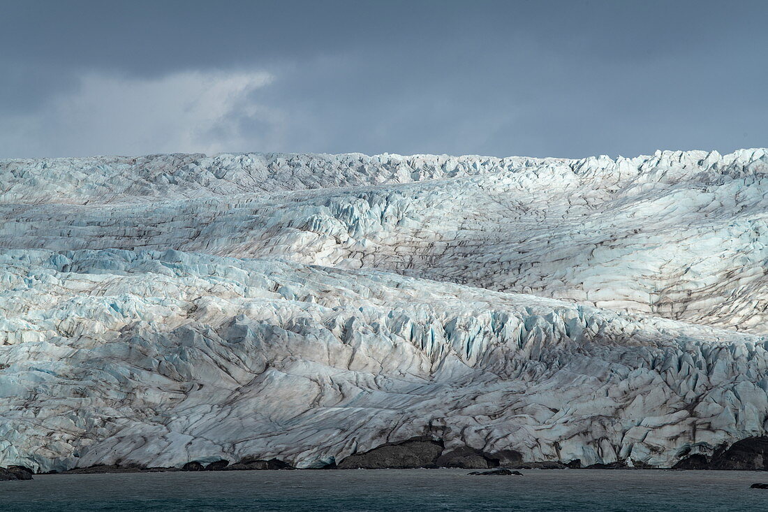 Sonnenlicht trifft auf die Oberfläche eines Gletschers, verursacht ein Lichtspiel und betont die schroffe Struktur, Billefjord, Spitzbergen, Norwegen, Europa