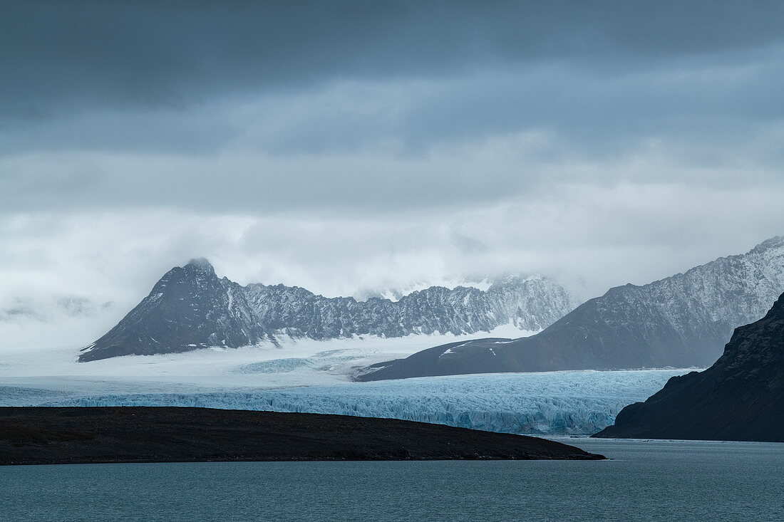 Graphic scene of rugged mountains and a long, wide glacier that stretches to the sea, Signehamna, Land Albert I, Spitsbergen, Norway, Europe