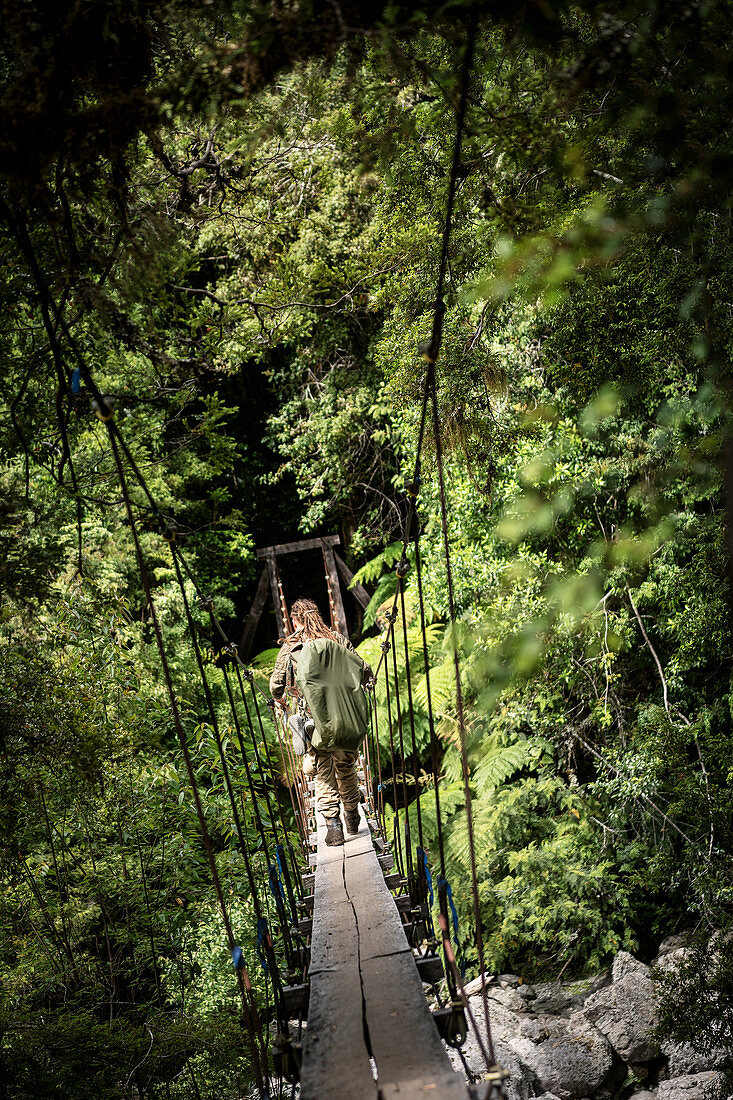Hiker crosses suspension rope bridge on the way to La Junta in the Cochamo Valley, Region de los Lagos, Chile, South America
