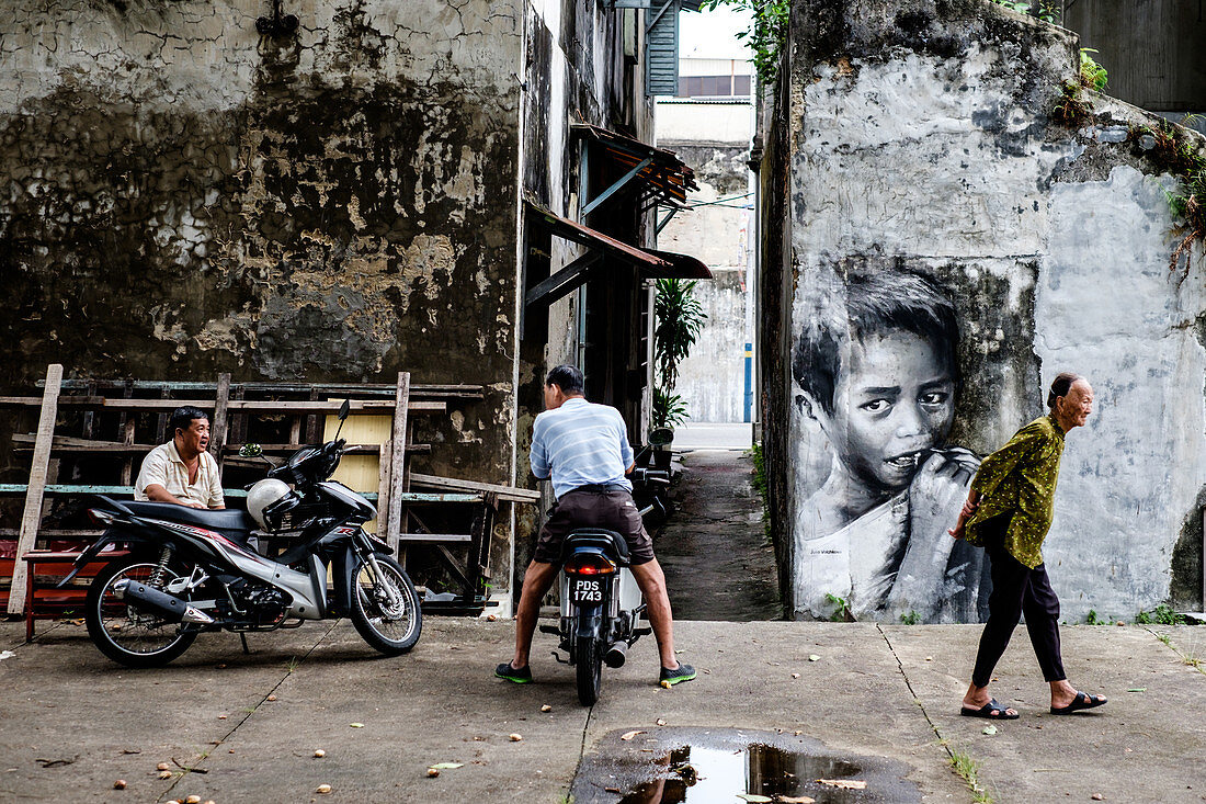 Penang, Malaysia - Junuary 19, 2015: An elderly person is passing two men, who are talking to each other.