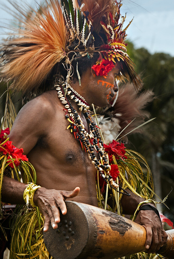 Papua New Guinea - November 8, 2010:  A man with tribal face painting and wearing special clothing is playing a Kundu Drum on a festival.