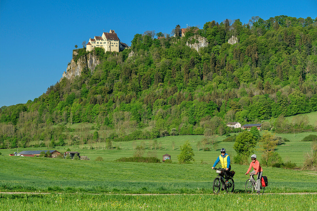 Man and woman ride a bike through the Upper Danube Valley, Werenwag Castle in the background, Upper Danube Valley, Danube Cycle Path, Baden-Württemberg, Germany