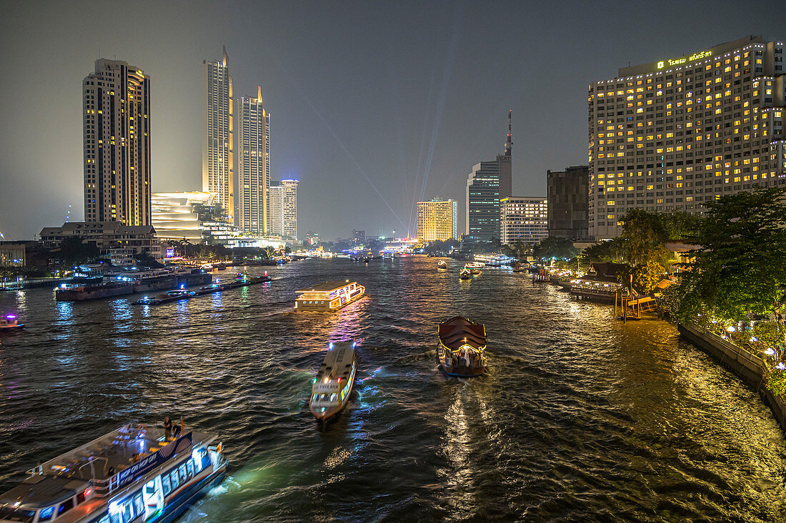 Blick von Taksin Brücke auf Boote und Hochhäuser bei Nacht, Bangkok, Thailand