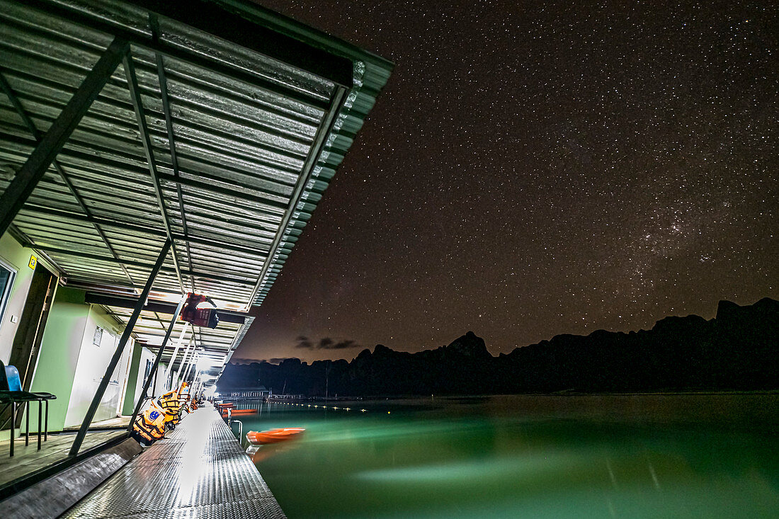 View over footbridge with bungalows (Khao Sok Smiley Lake House) at night with Milky Way, Ratchaprapha Lake, Khao Sok National Park ,, Thailand