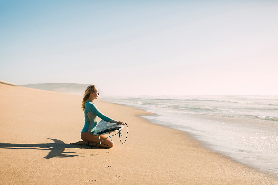 Woman kneeling holding surfboard on beach