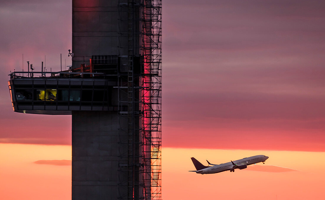 Airplane flying past control tower at sunset