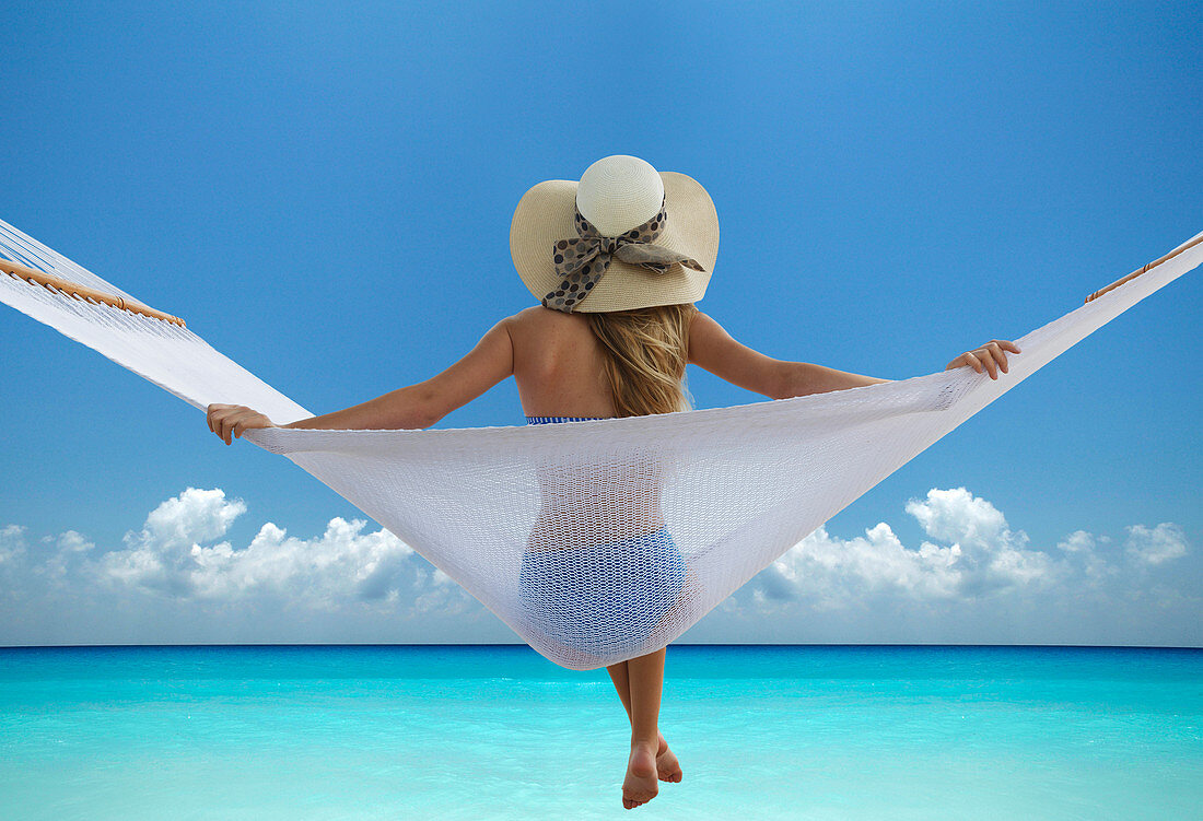 Frau sitzt in der Hängematte am Strand, Rückenansicht