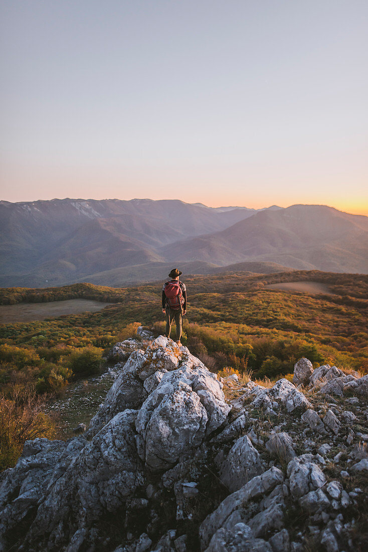 Man on rock by mountains at sunset