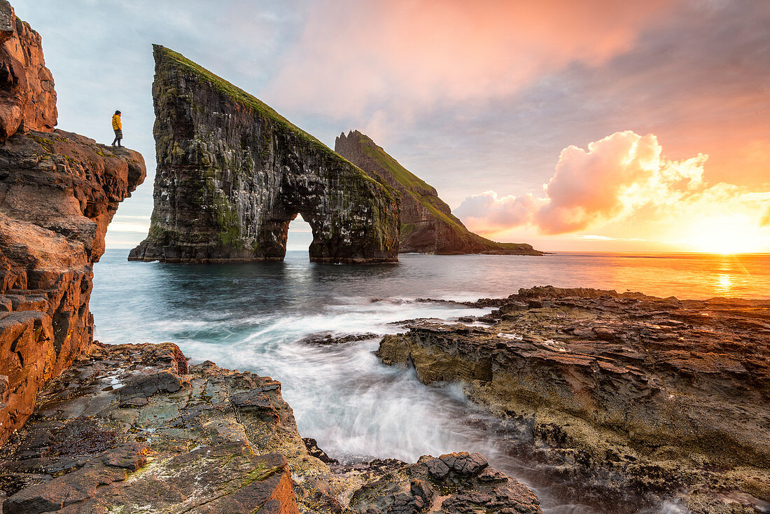 Wanderer bewundert den Sonnenuntergang vor dem Felsen von Drangarnir, Vagar Island, Färöer, Dänemark