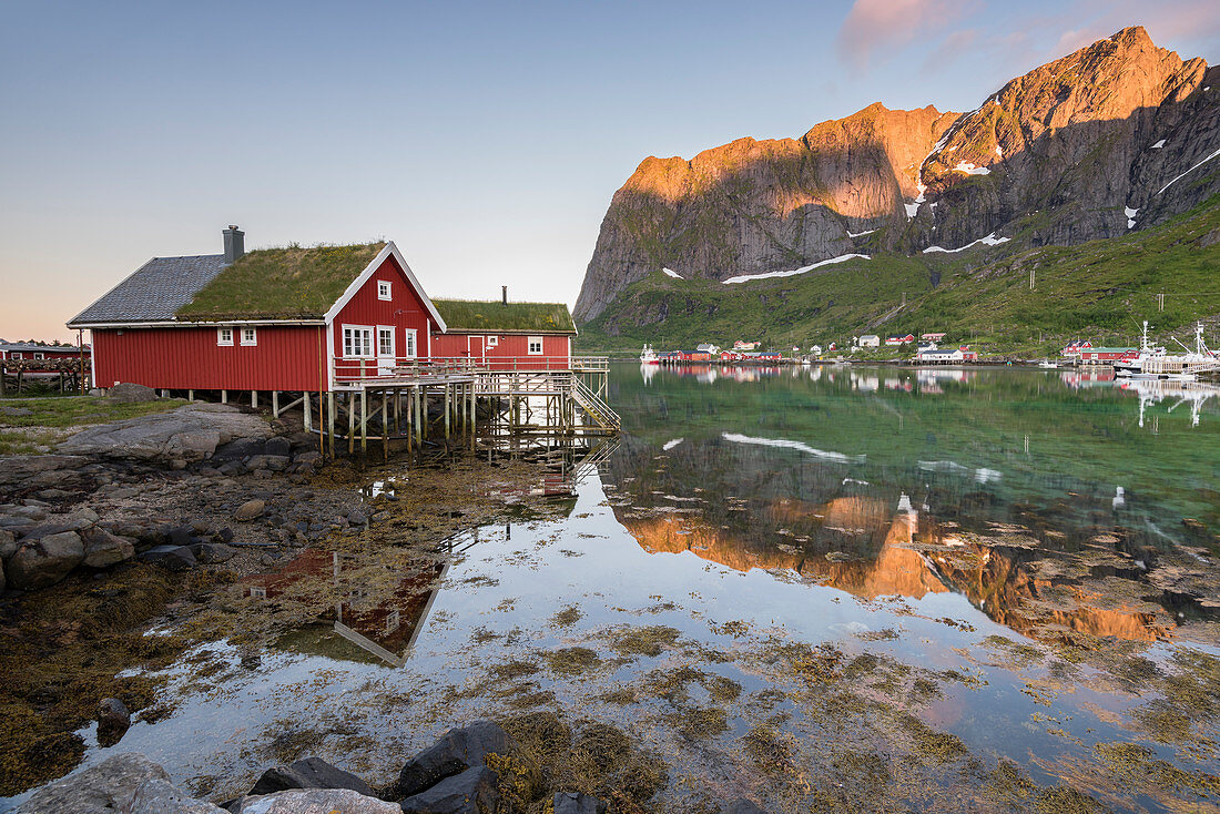 Das Fischerdorf und die Berge spiegeln sich im Wasser während der Mitternachtssonne, Reine, Provinz Nordland, Lofoten, Nordnorwegen, Europa