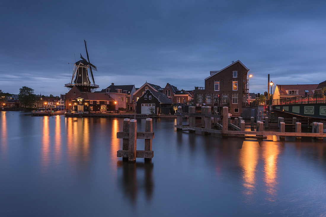 View of Windmill De Adriaan reflected in the canal of the river Spaarne during blue hour, Haarlem, Amsterdam district, Papentorenvest, Randstad, North Holland, The Netherlands, Europe