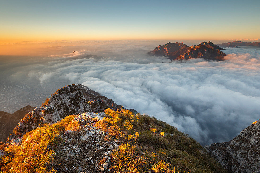 Sonnenaufgang über den Bergen von Lecco (Corni di Canzo, Rai, Moregallo), in Wolken gehüllt von der Spitze des Coltignone-Berges, Piani dei Resinelli, Provinz Lecco, Lombardei, Italien, Europa