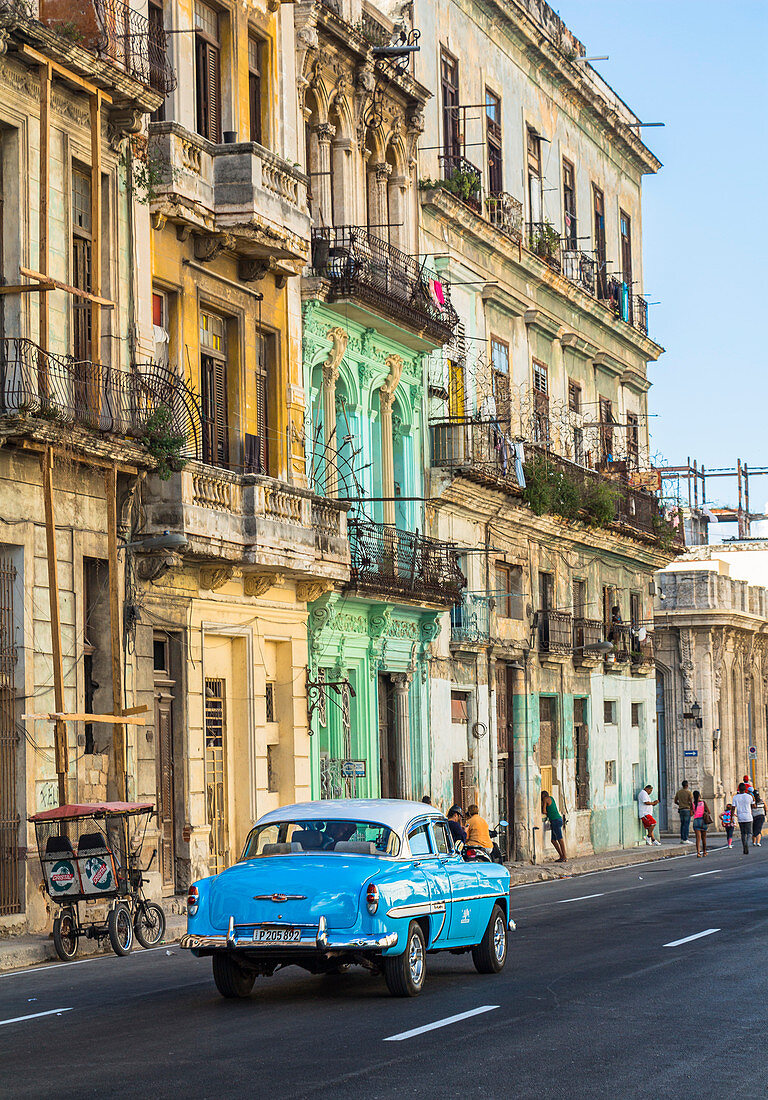Oldtimer fährt durch kubanische Straße mit alten, bunten Häuserfassaden im Kolonialstil, Altstadt von Havanna, Kuba