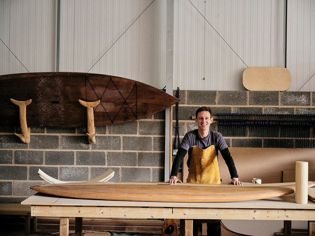 Mann mit einem handgemachten Paddleboard aus Holz in der Werkstatt