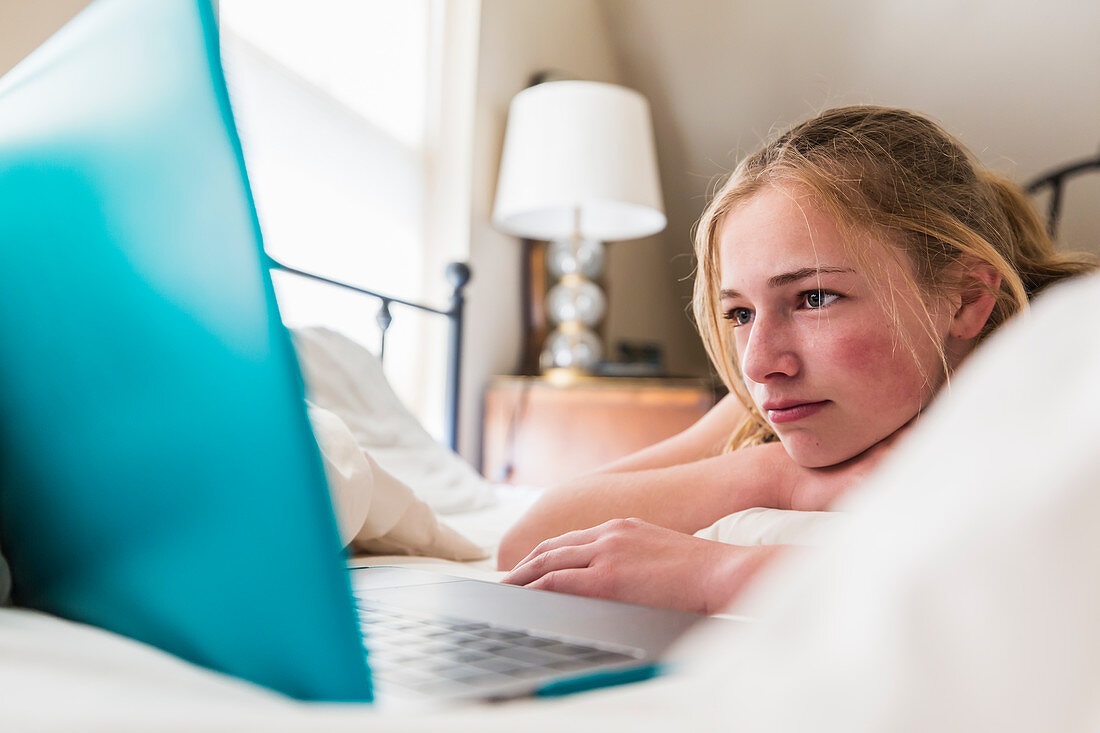 Teenager-Mädchen liegt vor einem Laptop im Bett