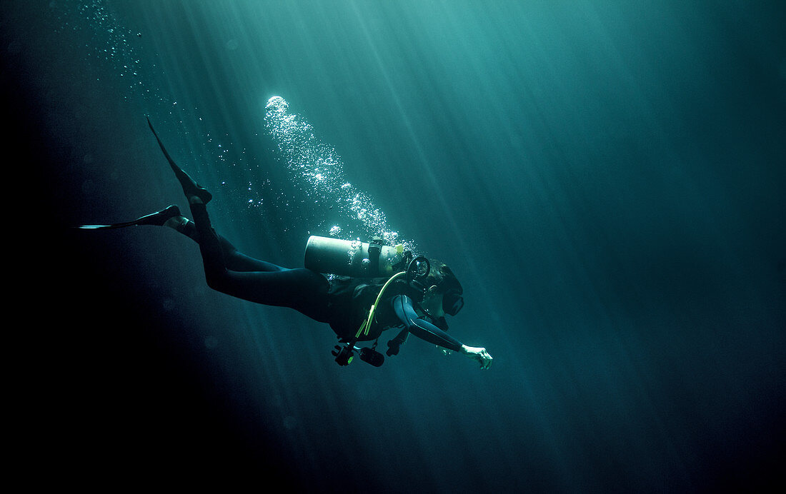 Unterwasseraufnahme eines Tauchers mit Neoprenanzug, Taucherbrille und Sauerstoffflasche, Luftblasen steigen auf
