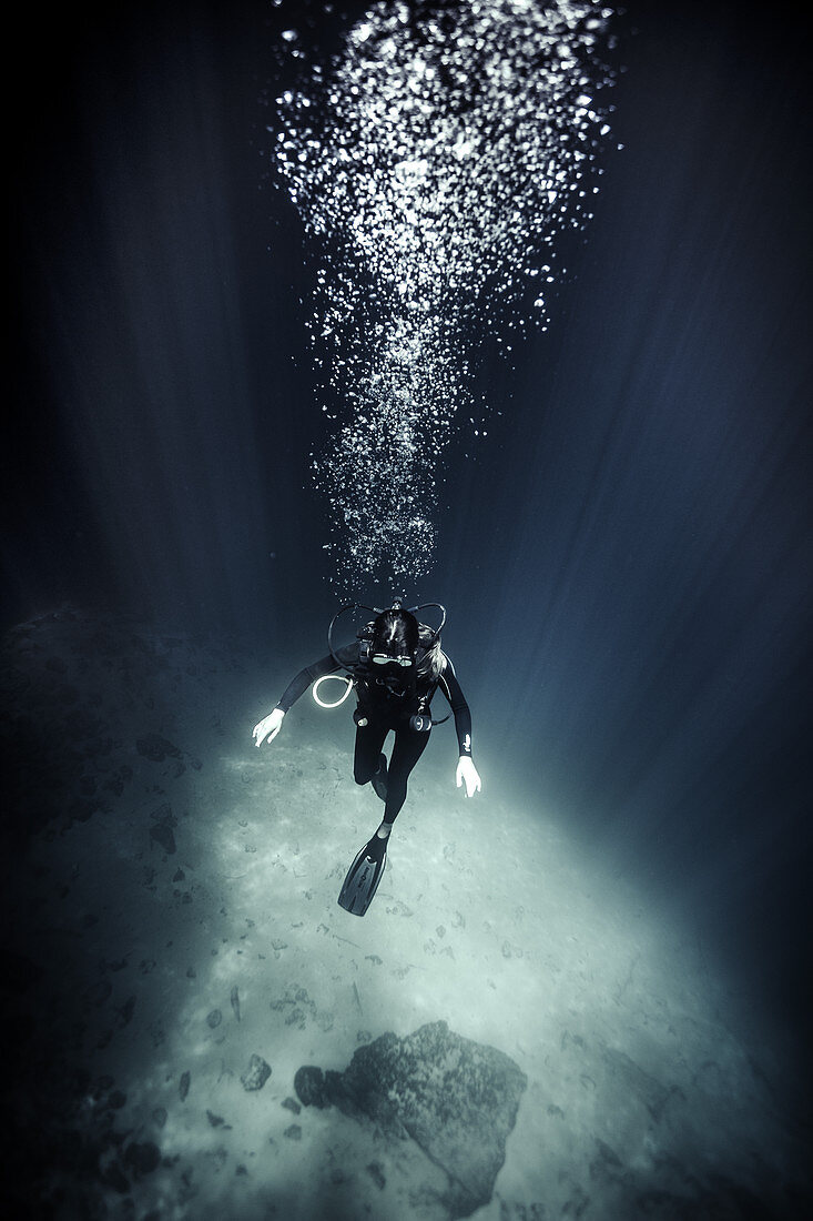 High angle underwater view of diver wearing wet suit and flippers, air bubbles rising.